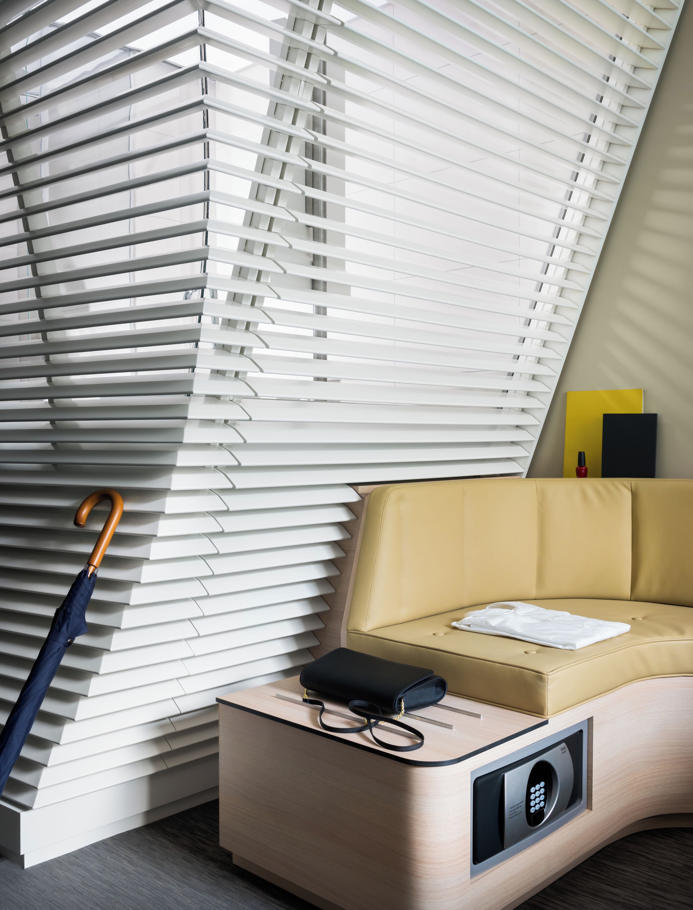 Una habitación moderna con un sofá curvo, un banco de madera y un altavoz fijado a la pared.