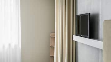A hotel room with a bed, a television on a wall, a pair of shoes, and a bag.