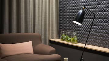 A modern living room with a brown sofa, a small round table with a magazine, a black floor lamp, and a shelf with decorative jars.