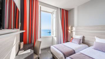 A hotel room with two beds, a desk, and a view of the sea.