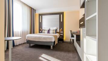 Habitación de hotel con cama, mesita de noche, silla, escritorio y armario empotrado.