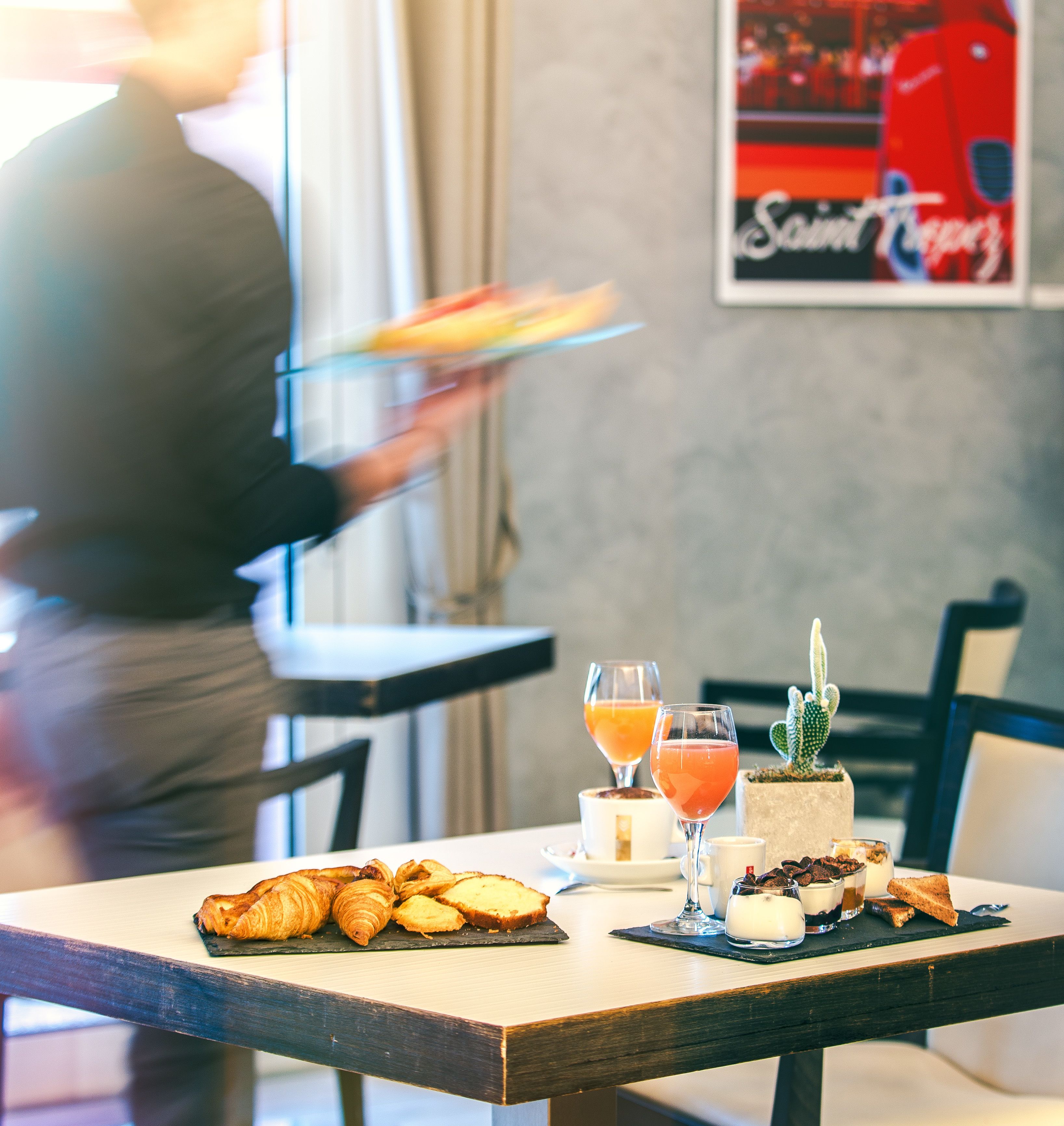 A dining table with pastries, drinks, and a dessert. A person is serving food in the background.