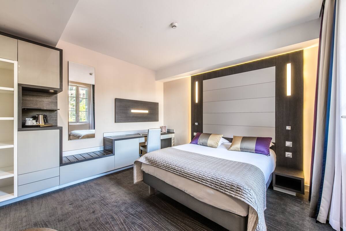 A modern hotel room with a large bed, built-in desk, and a large mirror.