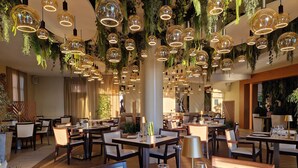 A restaurant with round tables, hanging spherical light fixtures, and indoor plants. - Le Saint Paul Hôtel (Nice)