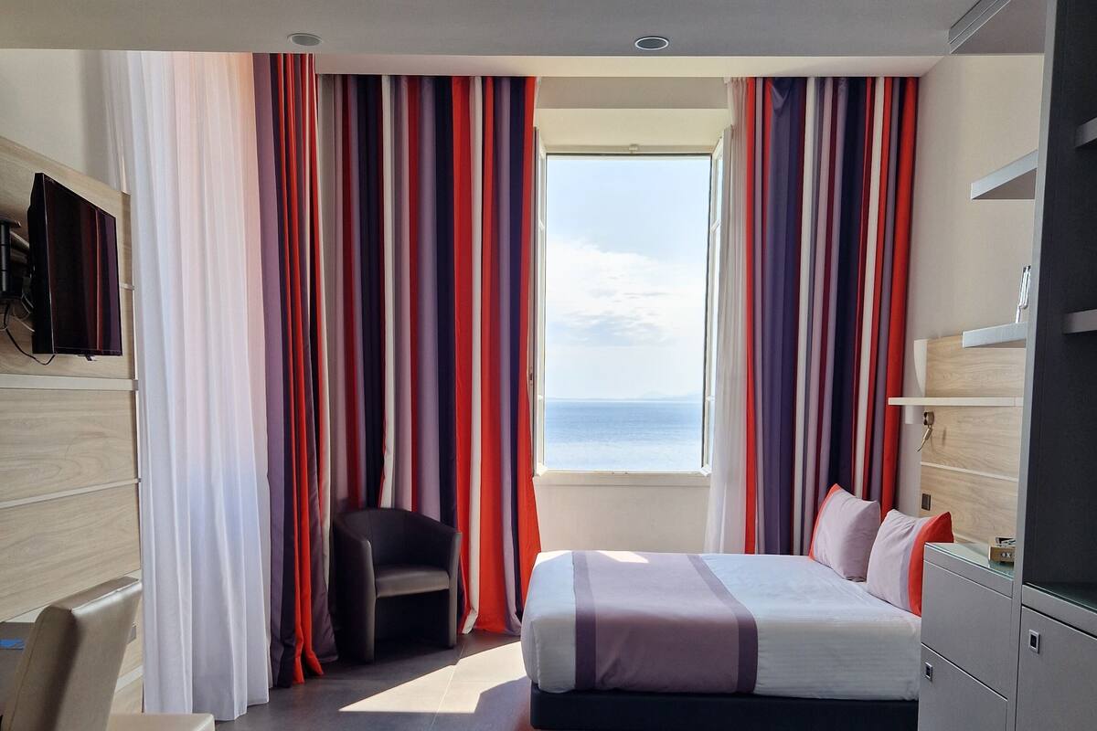 A modern hotel room with a bed, a desk, a chair, and a TV mounted on the wall.