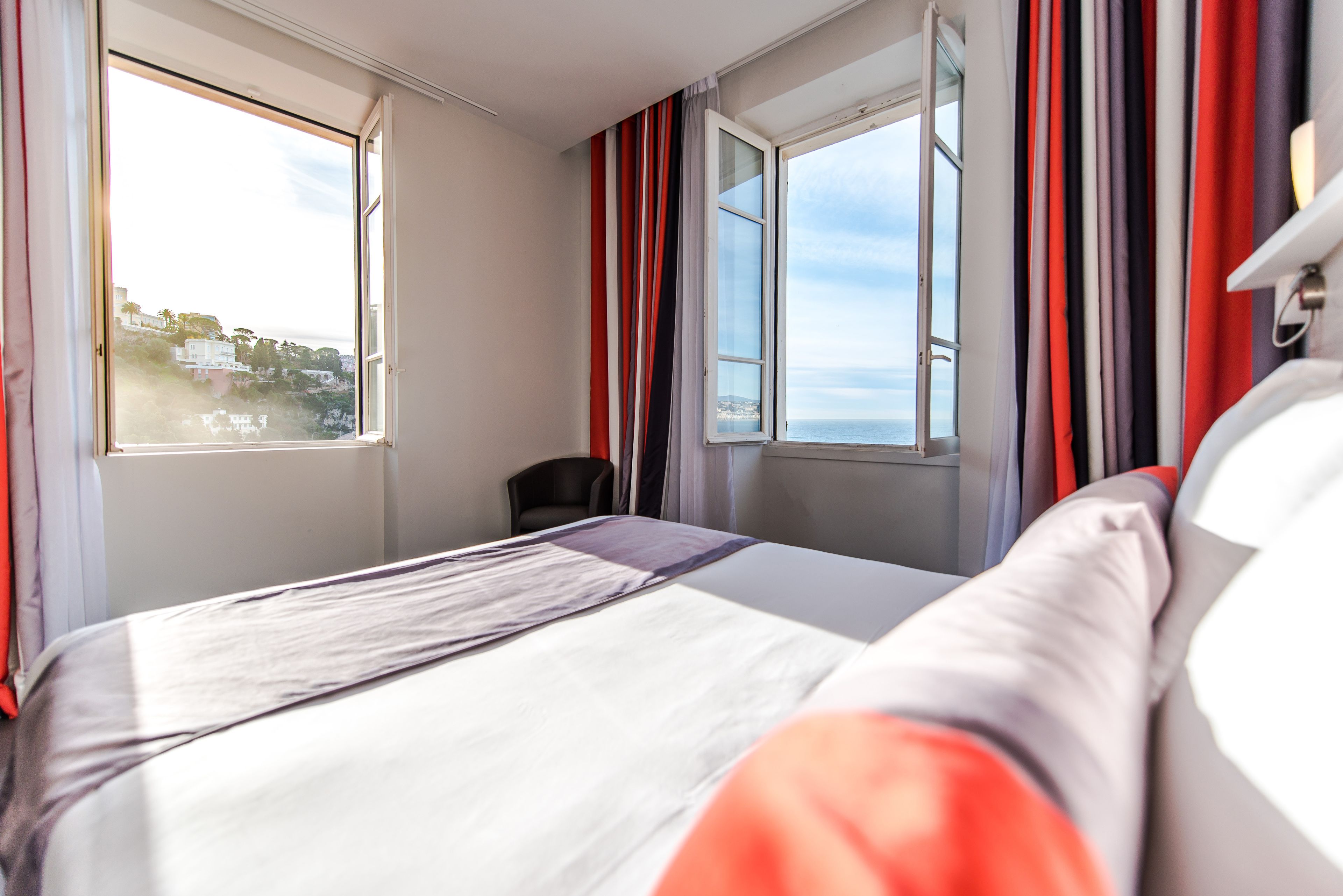 Quarto de hotel com uma cama, uma cadeira e vista para o mar.