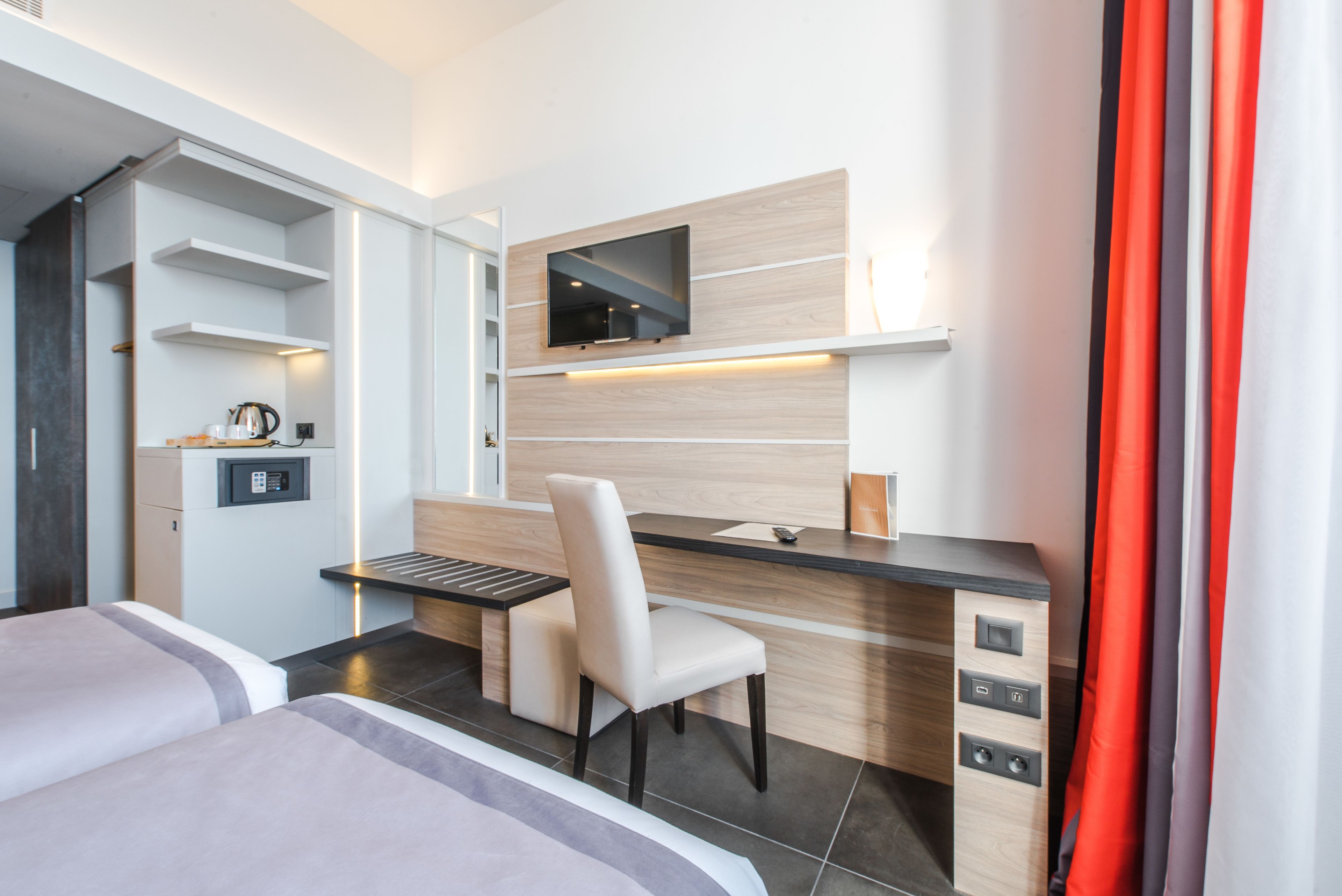Habitación de hotel moderna con cama, escritorio con silla, televisión de pantalla plana y estante empotrado con hervidor.