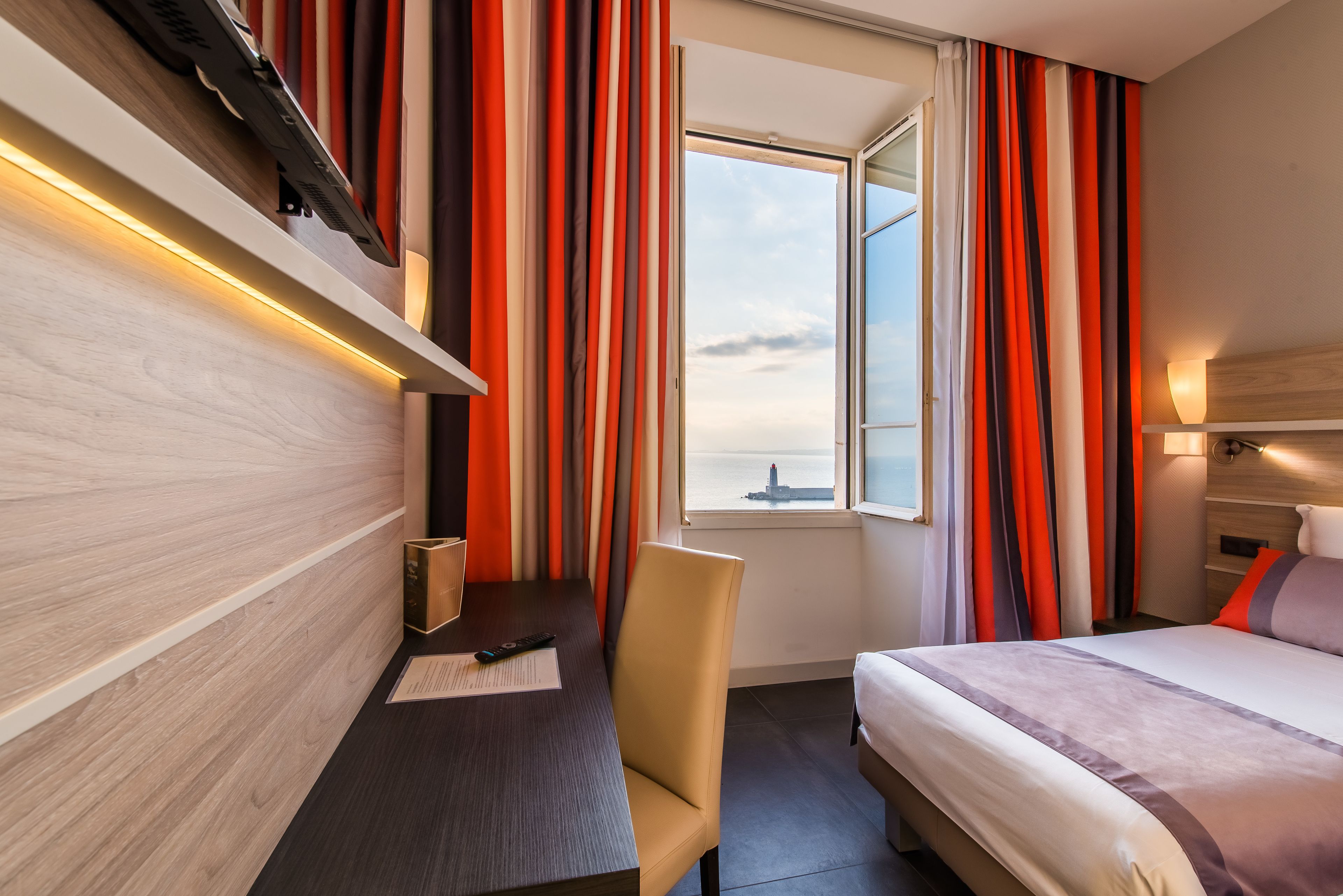 Habitación de hotel con cama, escritorio con silla, ventana con cortinas y vista al agua.