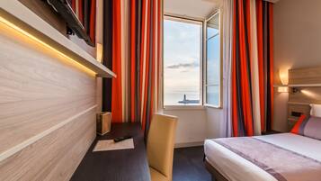 Habitación de hotel con cama, escritorio con silla, ventana con cortinas y vista al agua.