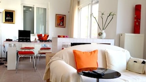 A modern living room with a white sofa, red chairs, a small black table, and a kitchen area in the background. - Amalia Residences (Marathon)