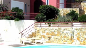 A multi-story building with balconies, a stone retaining wall, and a swimming pool. - Amalia Residences (Marathon)
