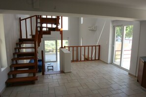 Un'ampia stanza con una scala in legno che conduce a un balcone, una porta scorrevole in vetro e un pavimento piastrellato.