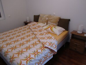 Un letto rifatto con cura, con copripiumino fantasia, due cuscini e un comodino con una lampada.