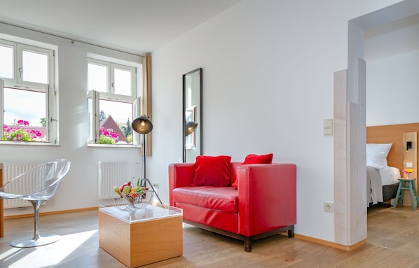 A modern living room with a red sofa, a clear chair, and a wooden coffee table. - Hezelhof Hotel (Dinkelsbuehl)