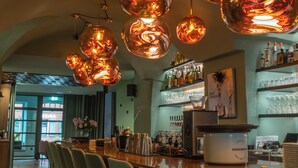 A bar area with multiple hanging copper-colored pendant lights, a bar counter, and several bar stools. - Hezelhof Hotel (Dinkelsbuehl)