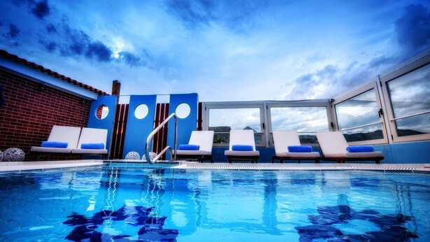 A poolside area with lounge chairs, a pool, and a view of the sky and mountains. - Hotel Lino Mare (Malevizi)