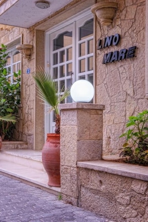 A stone building with a sign reading "LINO MARE" and a large potted plant in front. - Hotel Lino Mare (Malevizi)