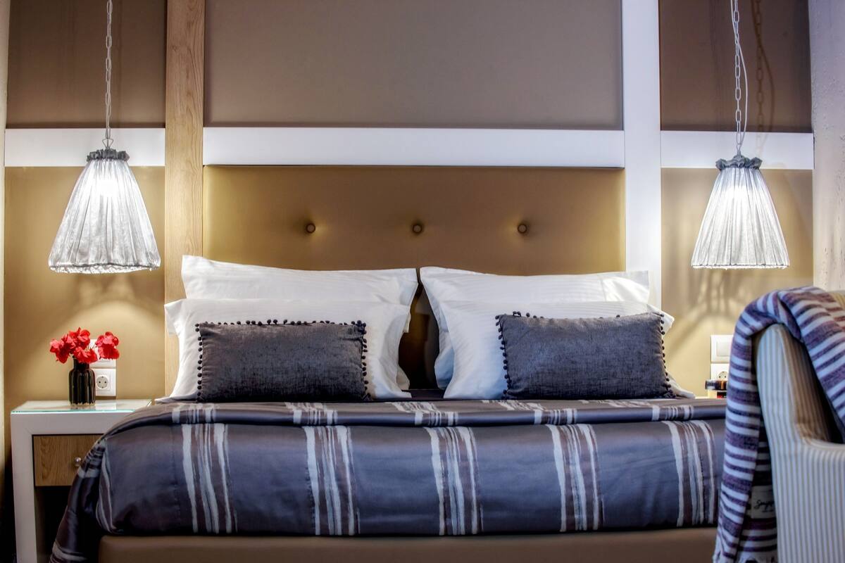 Uma cama bem arrumada com roupa de cama listrada, duas luminárias de cabeceira e um vaso com flores vermelhas na mesa de apoio.