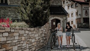 Dos personas junto a bicicletas sobre un camino empedrado, con muros de piedra y un edificio al fondo.