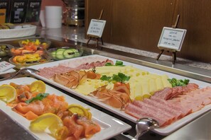 Un bufé con diversos alimentos, incluyendo salmón ahumado, jamón y queso.
