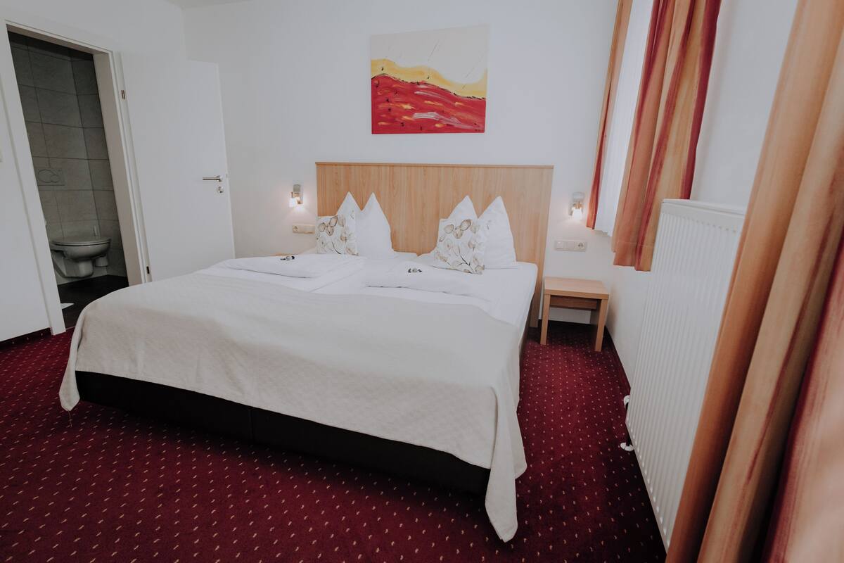 Een hotelkamer met een groot bed, een klein nachtkastje, een schilderij aan de muur en een radiator.