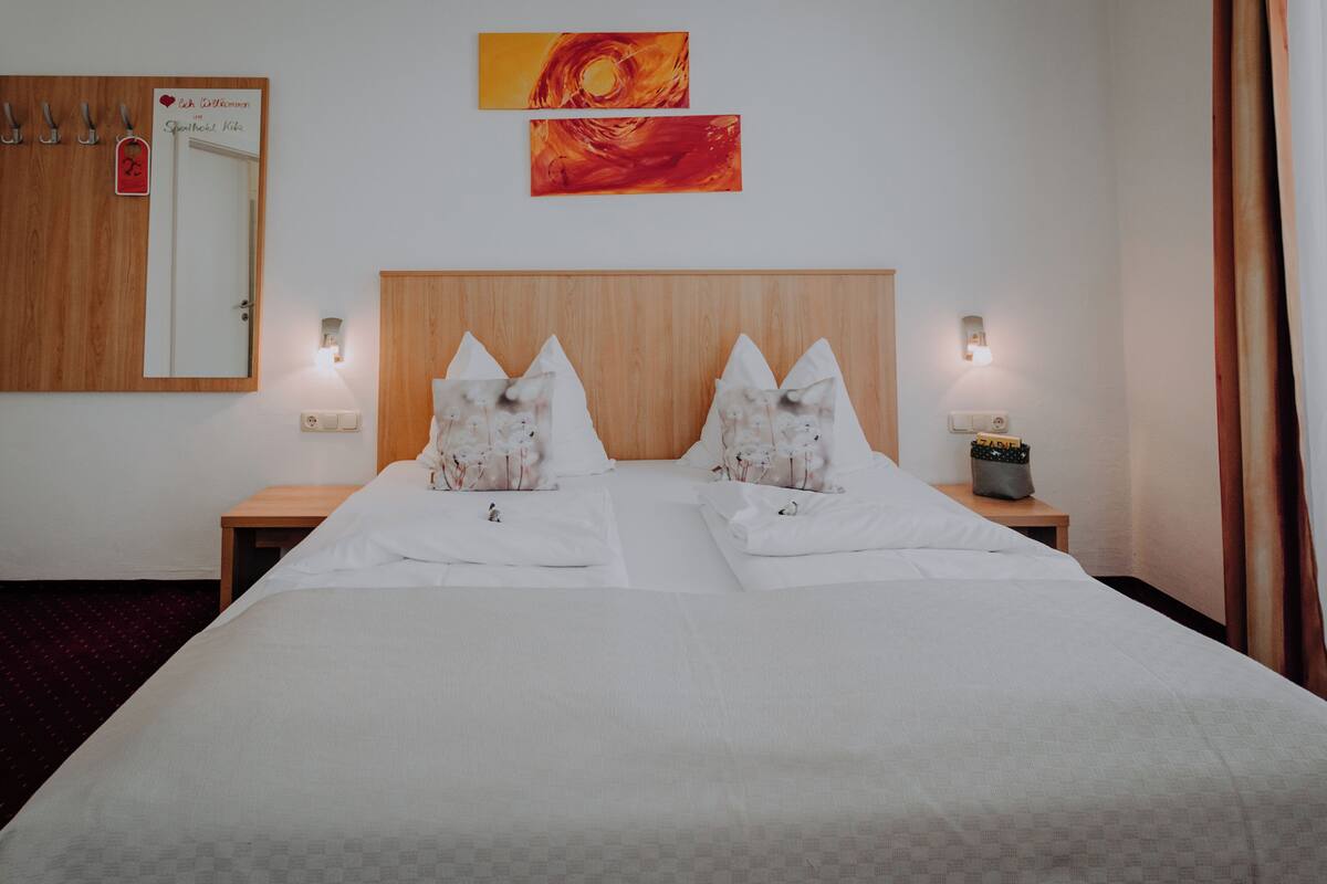 Een hotelkamer met een groot bed, twee nachtkastjes, een spiegel en twee aan de muur hangende schilderijen.