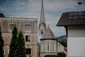 Una iglesia con una aguja alta y una torre del reloj, rodeada de edificios modernos con fachadas de madera y paneles solares.