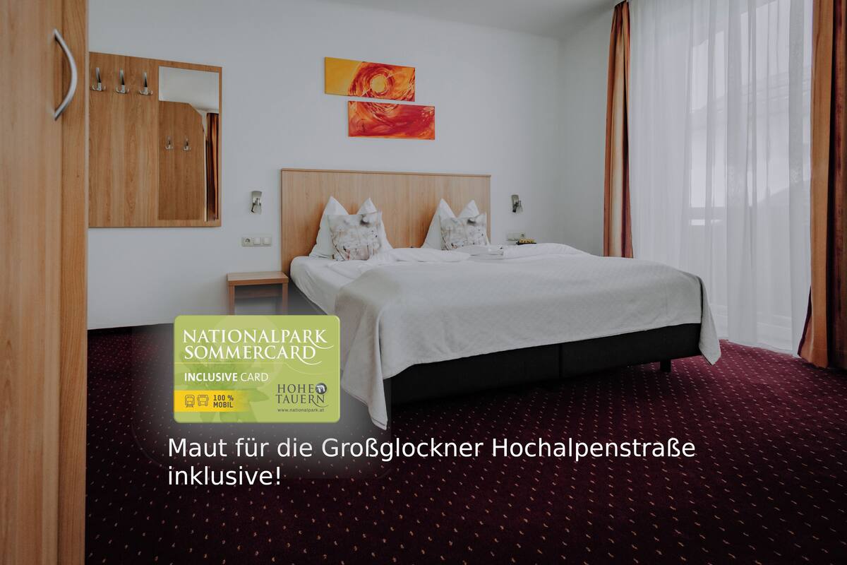 Een hotelkamer met een groot bed, een houten garderobe en een spiegel. Twee schilderijen hangen aan de muur en er is een raam met gordijnen.