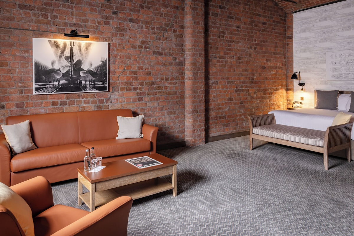 A room with a brick wall, a sofa, a bed, a coffee table, and a lamp.