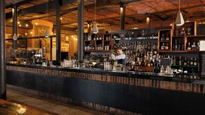 A bar with a bartender preparing drinks, shelves of liquor bottles, and a counter with various bar tools. - Titanic Hotel Liverpool (Liverpool)