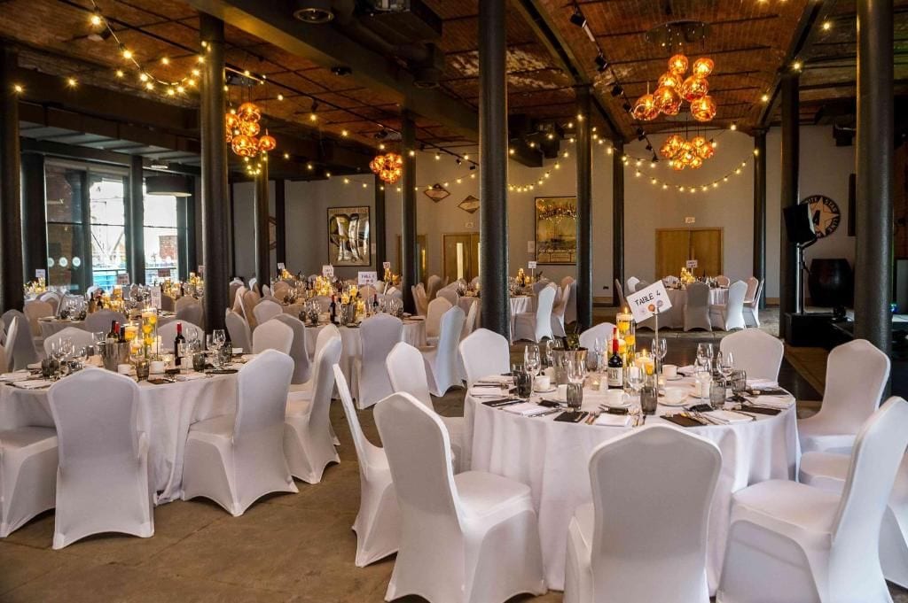 A banquet hall with round tables, white chairs, and string lights.