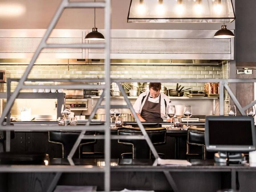A modern kitchen with stainless steel appliances, a chef preparing food, and a bar area with stools.