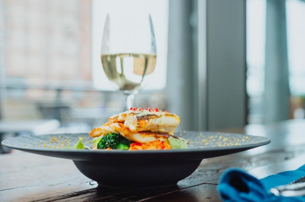 Un piatto di cibo con un bicchiere di vino bianco su un tavolo.