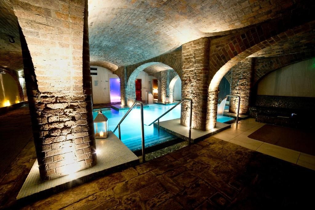 An indoor swimming pool with stone arches and a stone wall.