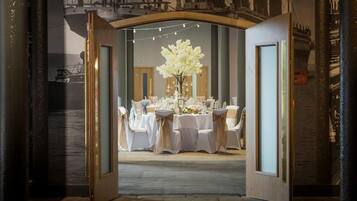 Un comedor interior con mesas dispuestas para una comida, un gran centro de mesa floral y vistas a un barco a través de un arco.