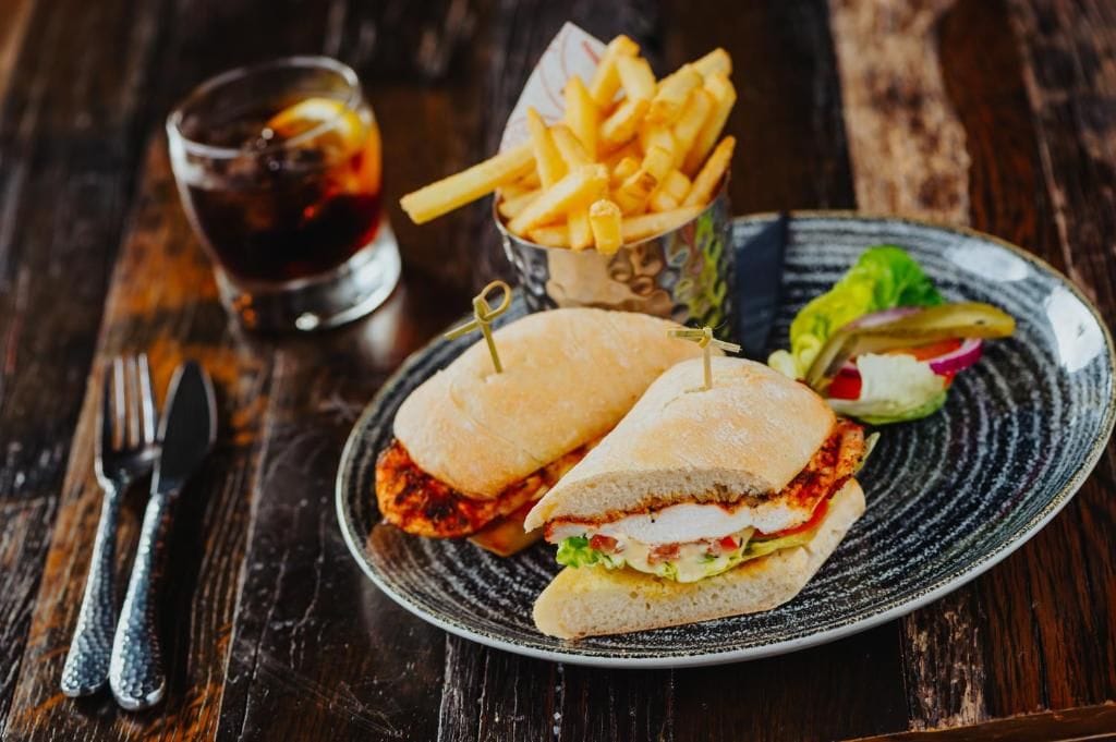 A sandwich with a side of fries and a drink on a plate.