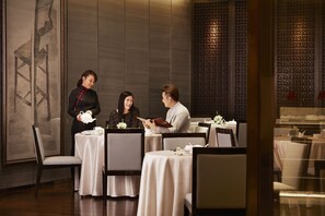 A restaurant with tables set for dining, a waiter attending to guests, and a decorative wall in the background. - Shanghai Marriott Hotel Parkview (Shanghai)