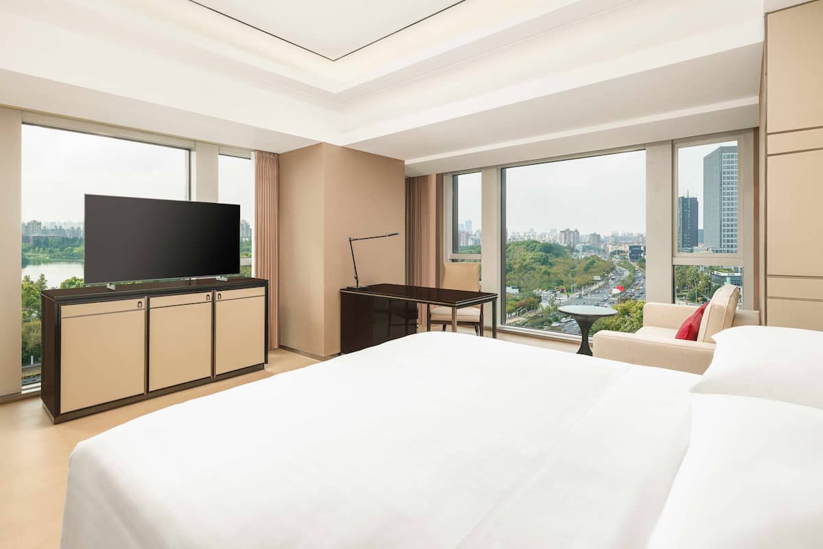 A modern hotel room with a large bed, a TV on a cabinet, a desk, and a sofa.