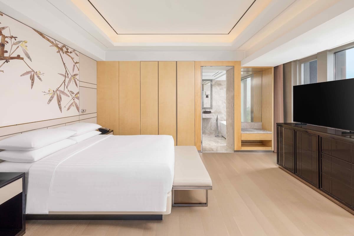 A modern hotel room with a large bed, a TV, and a wooden panel wall.