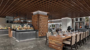 L’intérieur d’un restaurant moderne, avec une longue table à manger, des chaises, un pilier central et un espace cuisine en arrière-plan.