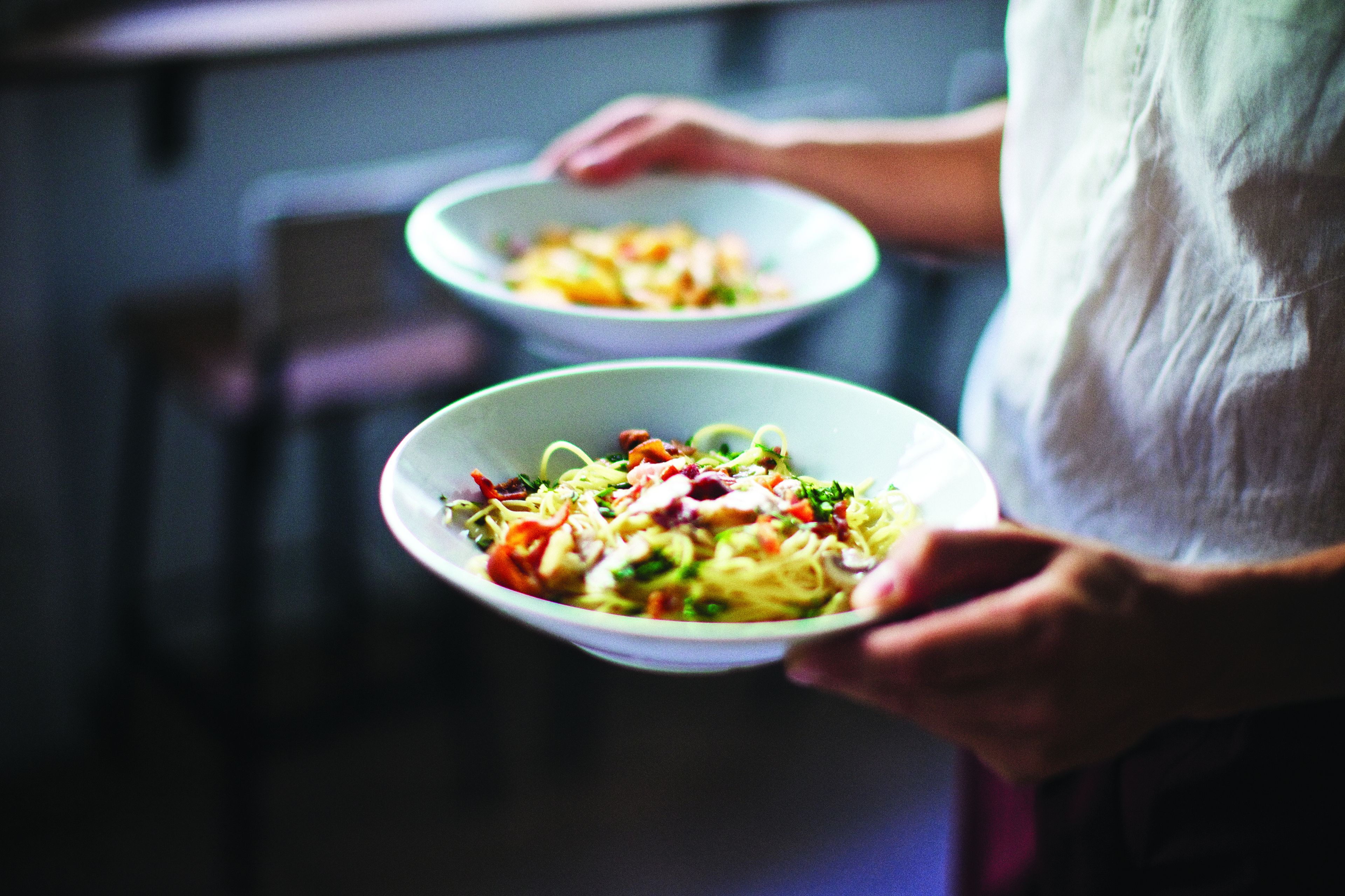 Twee porties pasta met groenten, vastgehouden door een persoon.