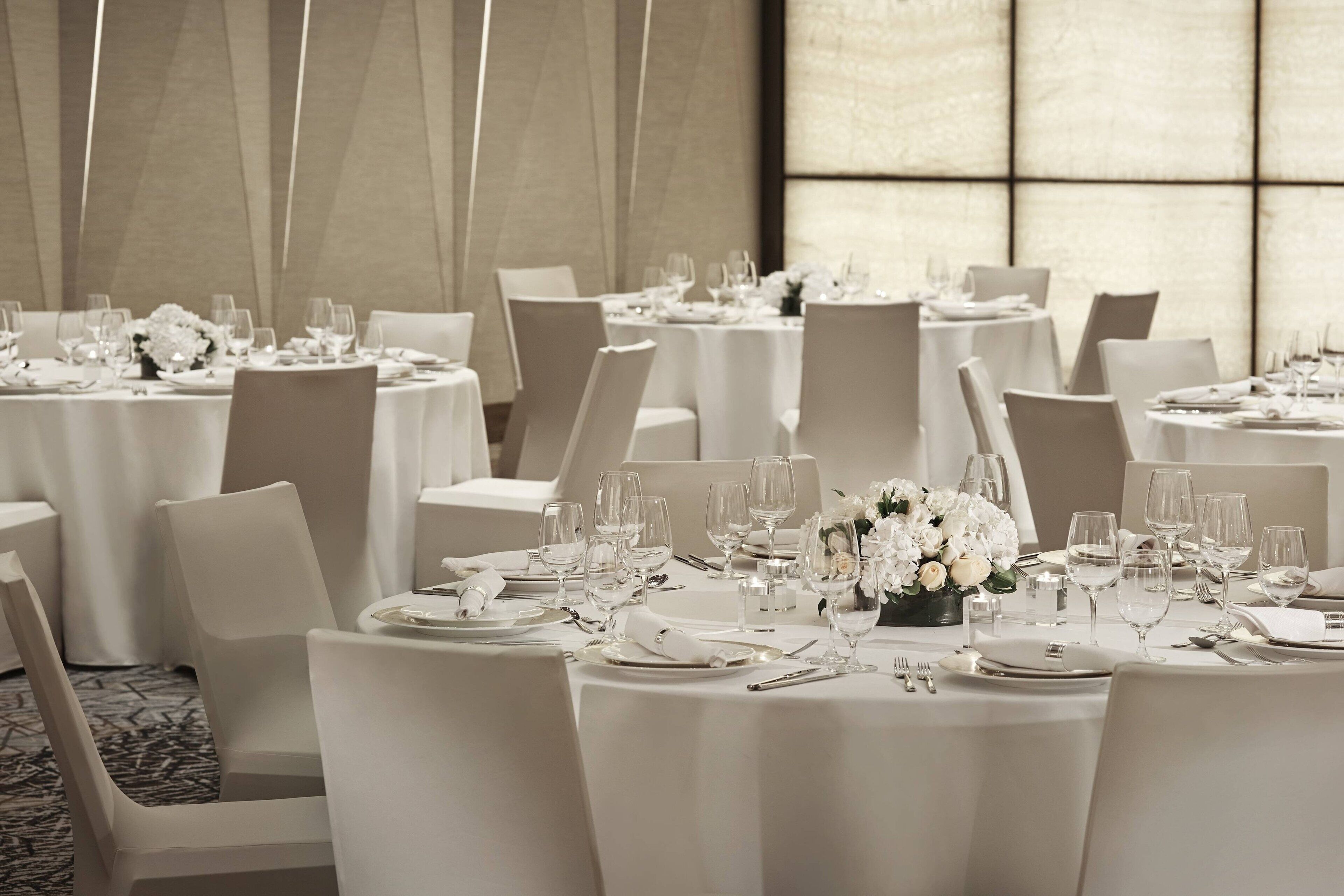 A banquet hall with round tables set for dining, each with white tablecloths, chairs, and glassware.