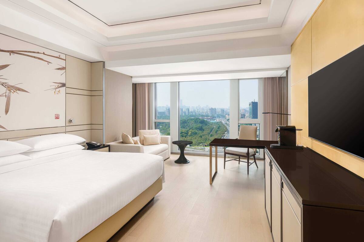 A hotel room with a large bed, a desk, a chair, and a TV.