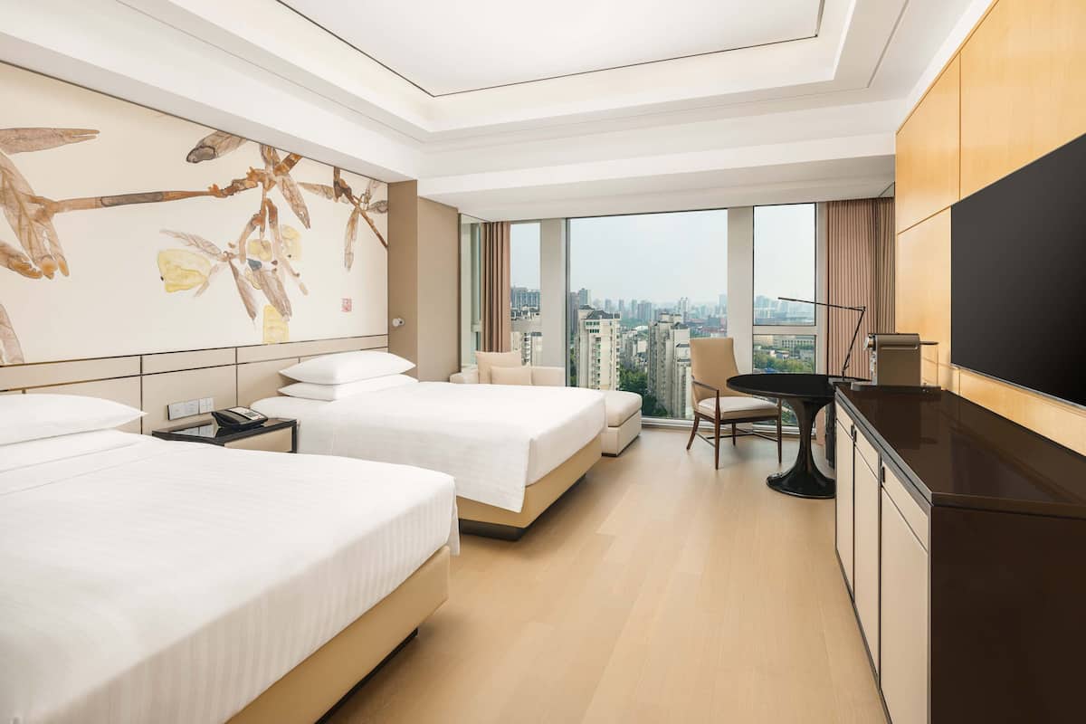 A hotel room with two beds, a dining area, a TV, and a city view.
