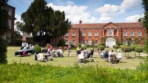 A spacious courtyard with a large brick building, outdoor seating, and a group of people gathered around tables. - Chicheley Hall (Newport Pagnell)