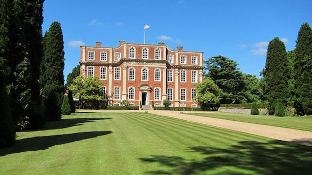 A large, symmetrical brick building with a central entrance, surrounded by a well-manicured lawn and tall trees. - Chicheley Hall (Newport Pagnell)