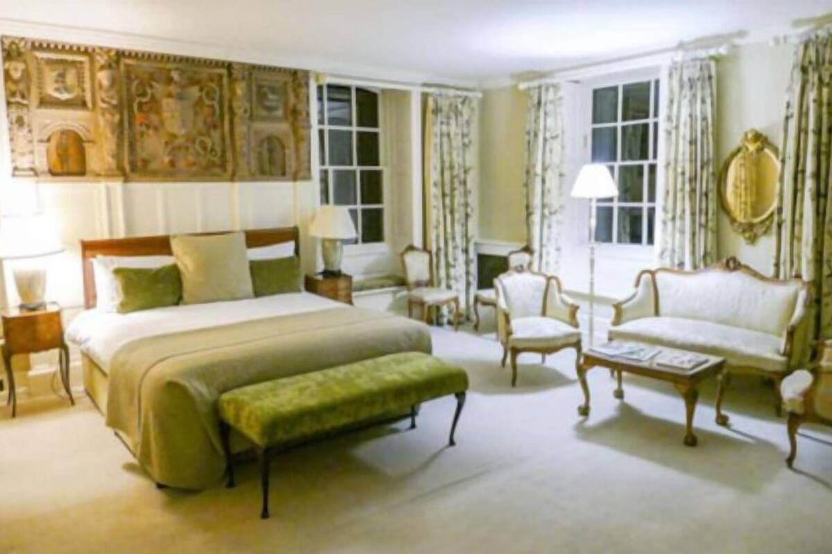 A spacious bedroom with a large bed, a sitting area with a sofa and chairs, and a decorative wall.
