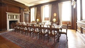 A formal dining room with a large wooden table set for a meal, flanked by tall chairs, a fireplace, and large windows with curtains. - Chicheley Hall (Newport Pagnell)