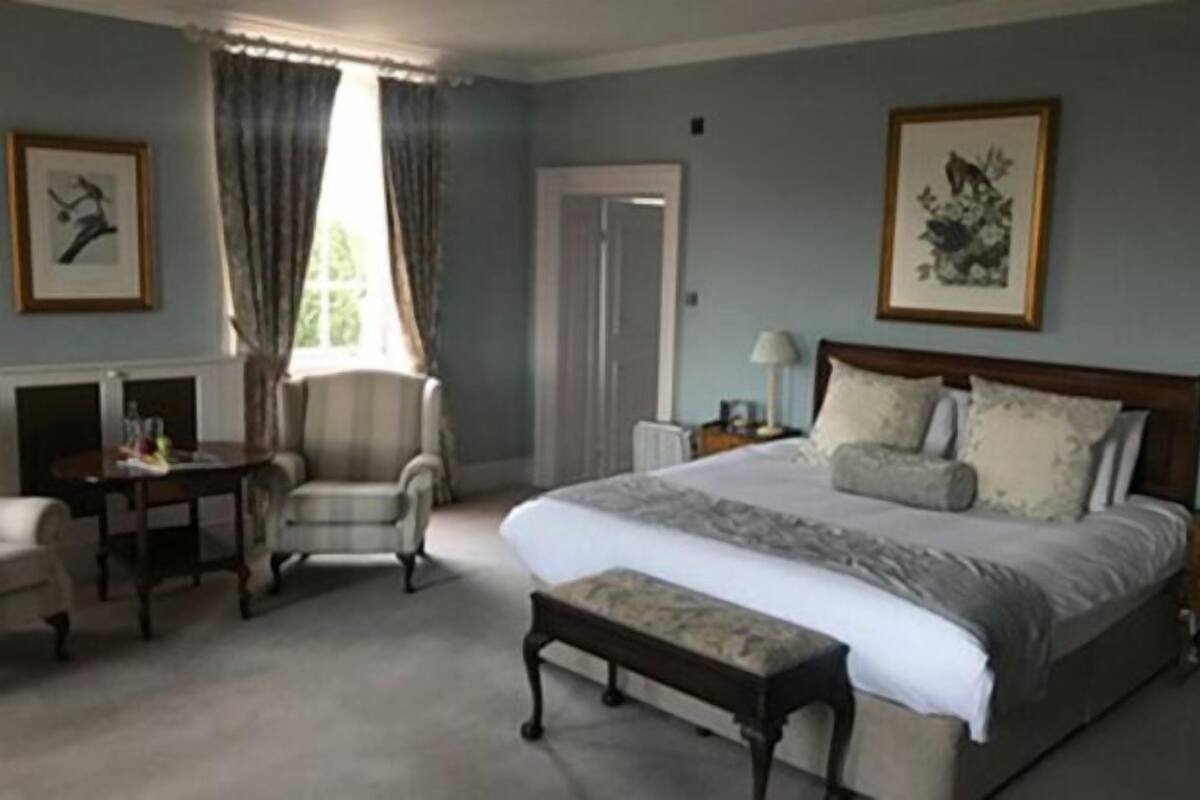 A bedroom with a large bed, a chair, a desk, and a window with curtains.