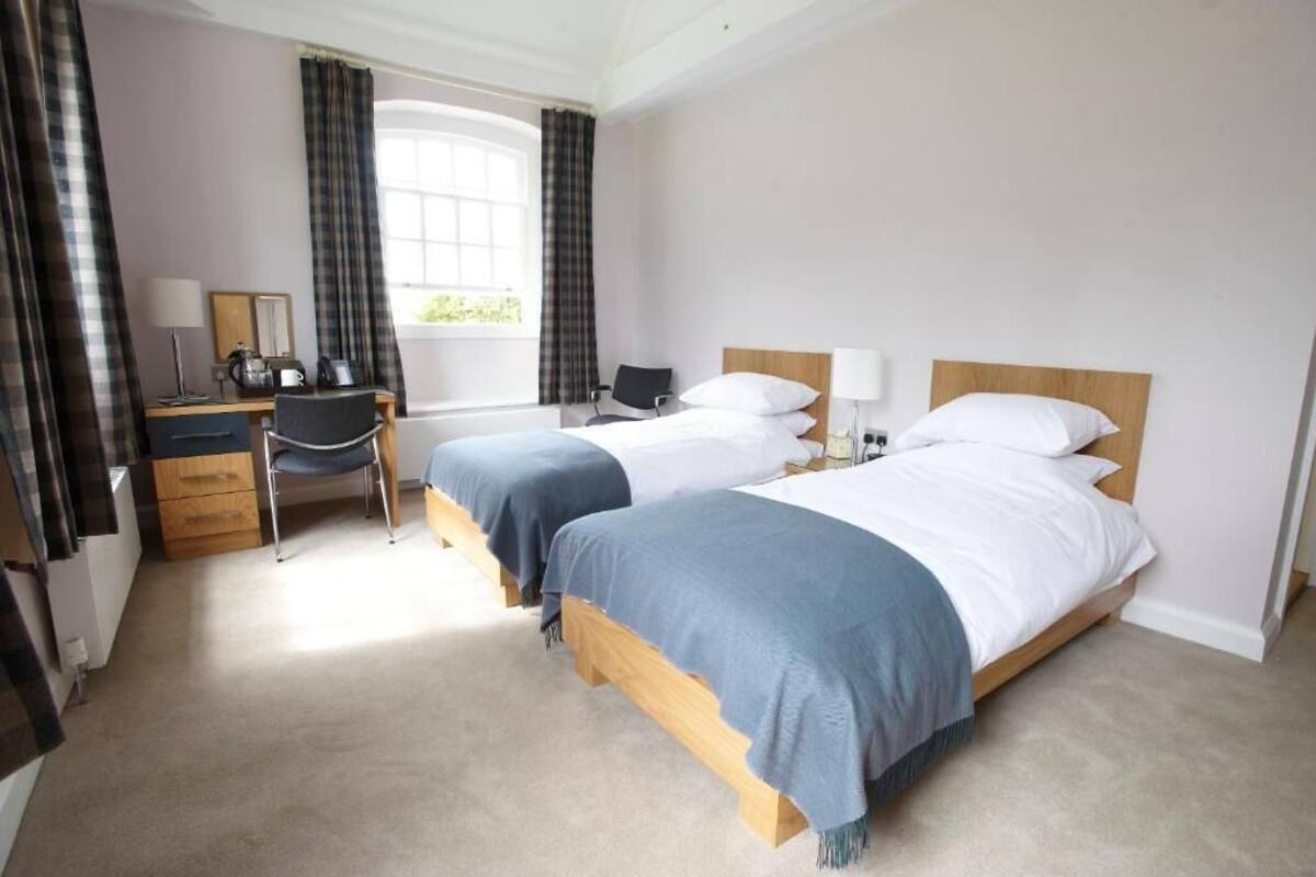 A hotel room with two beds, a desk with a chair, a window with curtains, and a carpeted floor.